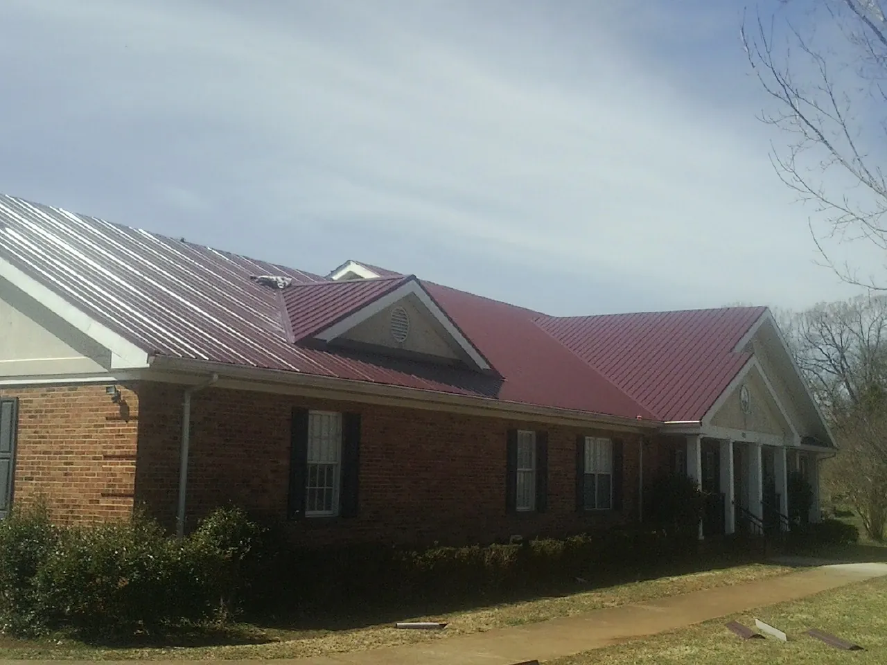 Red metal roof with gabled entries on a long brick building, from a Hail Damage Roof Repair job in Rives Junction