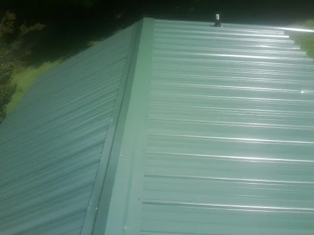 New green metal panels meeting at the ridge of a roof — Flat Roof Repair work by our crew in Rives Junction