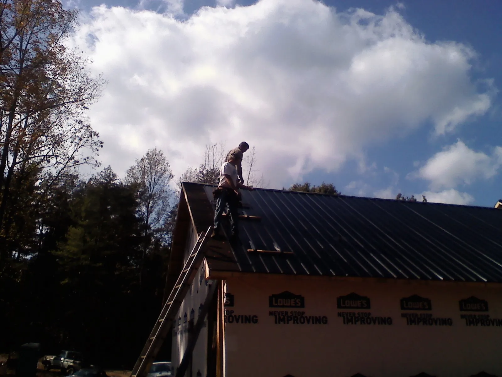 Roofer fastening dark metal panels high against a cloudy sky, from a Roof Inspection job in Rives Junction