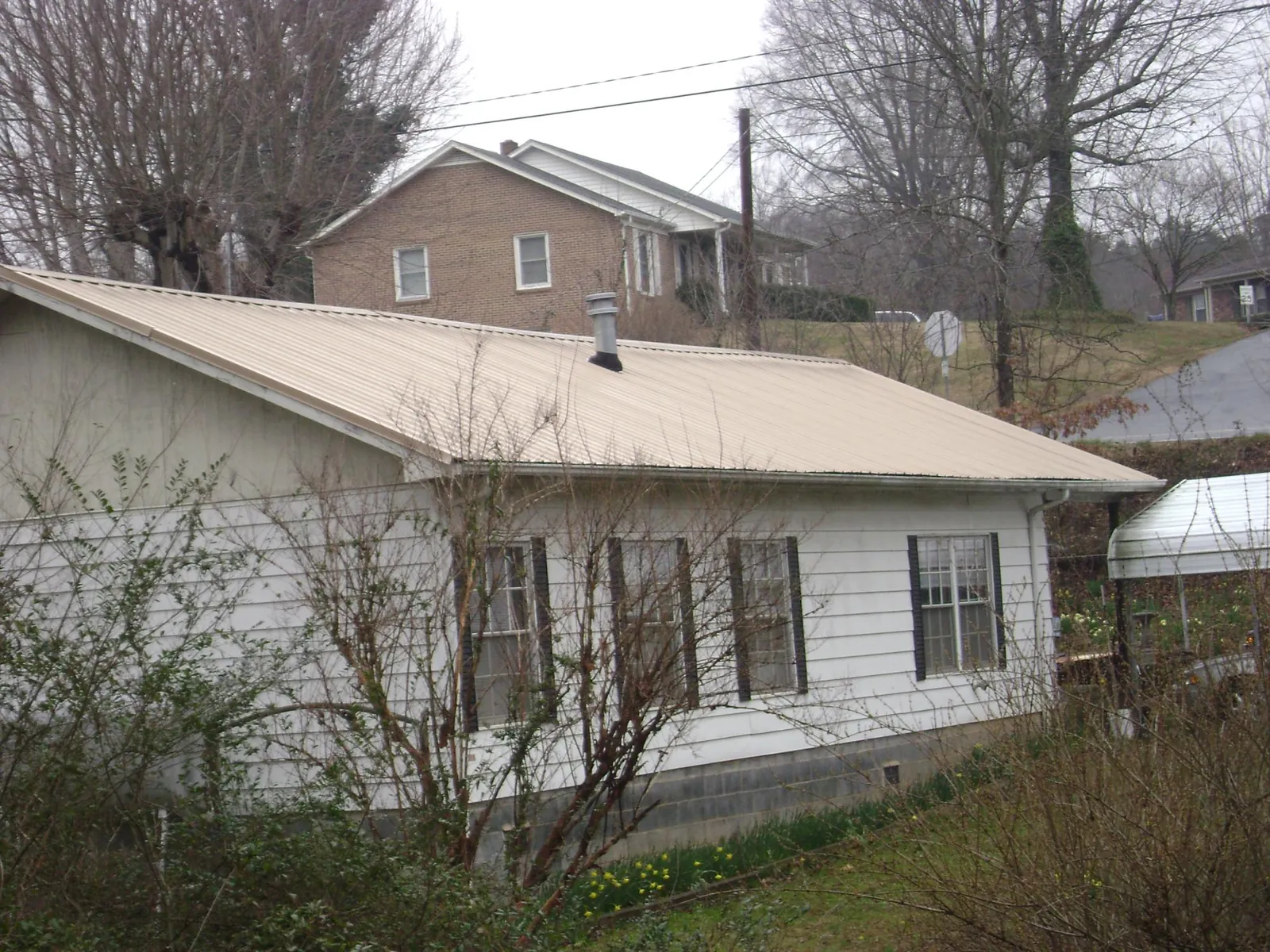 Tan metal roof on a white sided house set into a hillside — Commercial Roofing by Roofing Brothers in Rives Junction